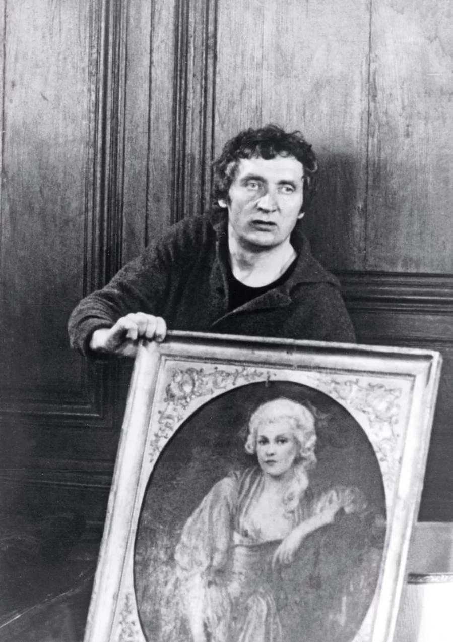 Black and white still of a man holding a framed oval portrait, from the cinema of Walerian Borowczyk